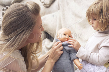 Mother and young daughter playing with baby doll together