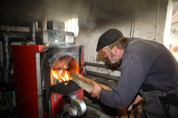 Prangendorf  Deutschland  Mann fuellt einen Holzvergaserofen mit Brennholz