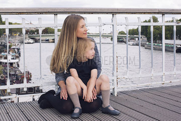 Mother and young daughter sitting together on bridge over canal