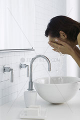 Woman leaning over bathroom sink washing face  side view