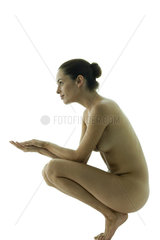 Nude woman crouching  hands clasped in front of her  side view