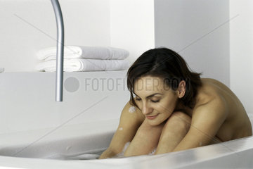 Woman sitting in bath with head resting on knees  eyes closed