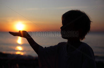 Kaegsdorf  Deutschland  Silhouette  ein Kind haelt eine Hand unter die untergehende Sonne