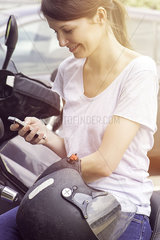 Woman sitting on motorcycle  smiling at smartphone