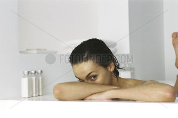 Woman in bathtub  resting head on arms  peeking at camera