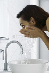Woman leaning over sink washing face  side view