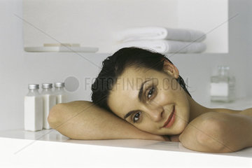 Woman in bath  resting head on arms against side of tub