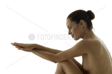 Nude woman sitting  looking at clasped hands  side view
