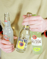 Junger Mann haelt verschiedene Alcopops Flaschen