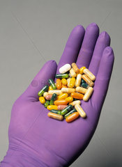 Tabletten in einer Hand  die einen farbigen OP-Handschuh traegt