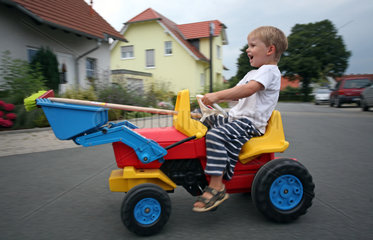 Werl  Deutschland  Junge faehrt lachend mit einem Spielzeugbagger auf der Strasse