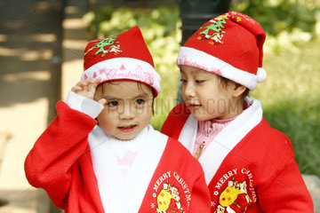 Zwei Kinder in Nikolauskostuemen in einem Park von Hanoi