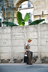 Havanna  Kuba  ein alter Mann mit Beuteln geht an der Absperrung eines baufaelligen Hauses vorbei