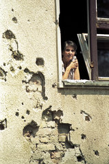 Sarajevo  Bosnien und Herzegowina  Frau schaut aus einem beschaedigten Haus