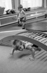 Berlin  DDR  Kind krabbelt in einer Kindertagesstaette unter einem Holzgitter durch