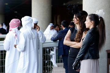 Dubai  Vereinigte Arabische Emirate  Maenner in Landestracht und elegant gekleidete Frauen mit Hut beim Pferderennen