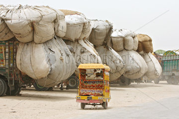 Hyderabad  Pakistan  LKWs beladen mit Reisspreu  im Vordergrund faehrt ein Tuk Tuk