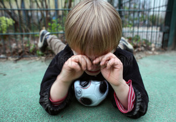 Berlin  Deutschland  kleiner Junge mit Fussball liegt weinend auf dem Boden