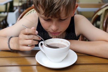 New York  USA  Junge loeffelt lustlos in einer Tasse mit Kakao