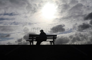 Hannover  alter Mann sitzt vor dramatischem Wolkenhimmel auf einer Bank