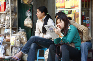 Frauen sitzen vor einem Geschaeft in der Altstadt von Hanoi