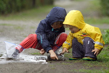 Berlin  Kinder in Regenkleidung spielen in einer Pfuetze