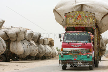 Hyderabad  Pakistan  LKWs beladen mit Reisspreu  im Vordergrund faehrt ein Tuk Tuk