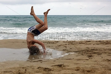 Noto  Italien  Junge laesst sich am Strand von Calamosche in eine Pfuetze fallen