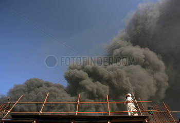 Dubai  VAE  Bauarbeiter auf einem Geruest vor schwarzer Rauchwolke