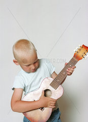 fuenfjaehriger Junge spielt Gitarre