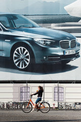 Berlin  Deutschland  eine Fahrradfahrerin faehrt an einem Grossplakat von BMW vorbei