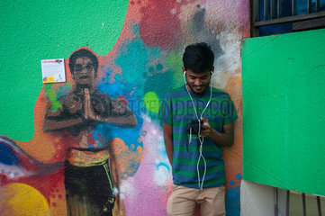 Singapur  Republik Singapur  Junger Mann steht vor einem Wandbild in Little India