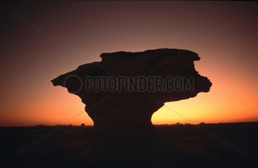 Silhouette eines pilzfoermigen Felsens bei Sonnenuntergang