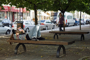 Berlin  Deutschland  eine junge Frau liegt auf einer Sitzbank und liest ein Buch