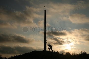 Pilger neben Gipfelkreuz bei Sonnenuntergang am Jakobsweg - Camino de Santiago