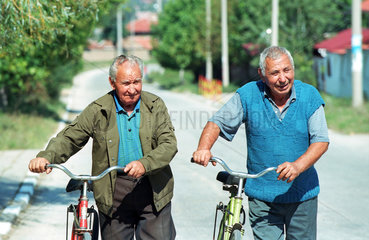 Zwei Maenner mit Fahrraedern an einer Dorfstrasse  Bulgarien