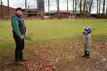 Mann mit Harke fuehrt Gespraech mit seinem Sohn im Garten  Norddeutschland
