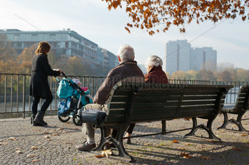 Berlin  Deutschland  Rentner auf einer Parkbank  Mutter mit Kinderwagen geht vorbei