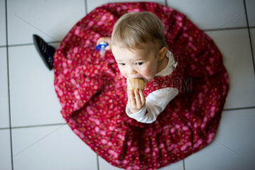 Berlin  Deutschland  18 Monate altes Maedchen sitzt in der Kueche und isst ein Broetchen