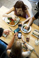 Group of friends sitting together in restaurants  all looking at smartphones