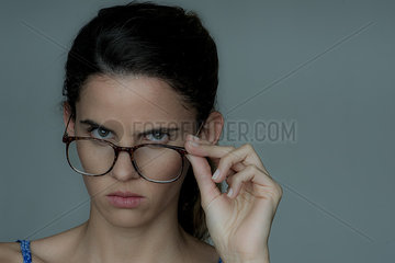 Young woman looking over the top of her eyeglasses  frowning  portrait