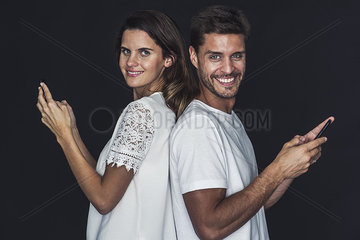 Couple back to back  both holding cell phones and smiling cheerfully