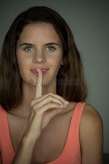 Young woman smiling with finger held to lips