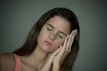 Young woman resting head on hands with eyes closed