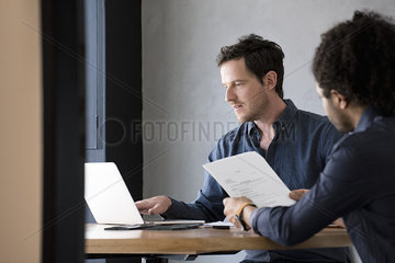 Man using laptop while other man reads document