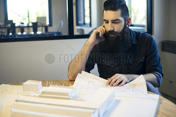 Architect looking at blueprints and talking on cell phone in office