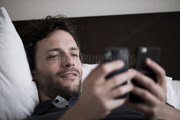 Man reclining in bed looking at two smart phones