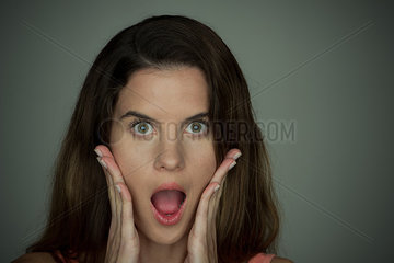 Young woman with surprised expression on face and hands on cheeks  portrait