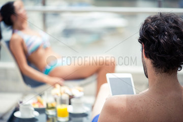Man relaxing by pool using digital tablet