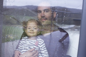 Man with young child looking through window watching rain fall